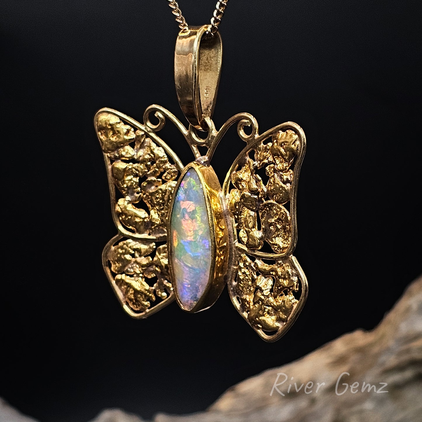 Gold butterfly pendant with opal stone on a dark background