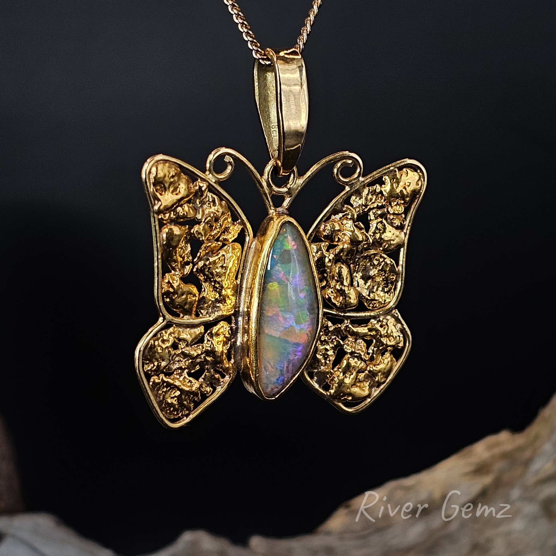 Gold butterfly pendant with opal center on a dark background, featuring 'River Gemz' branding.