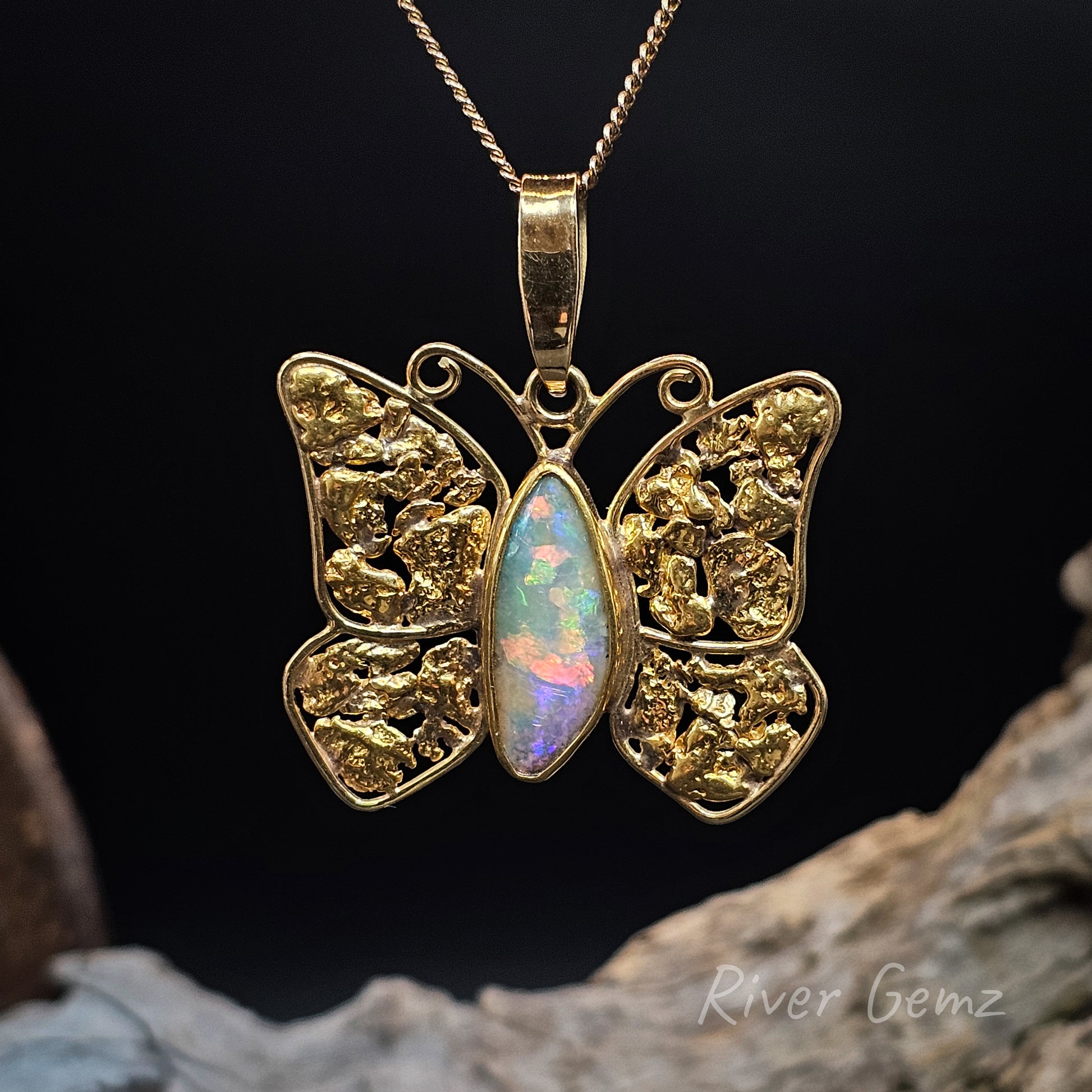 Gold butterfly pendant with a colorful boulder opal on a dark background