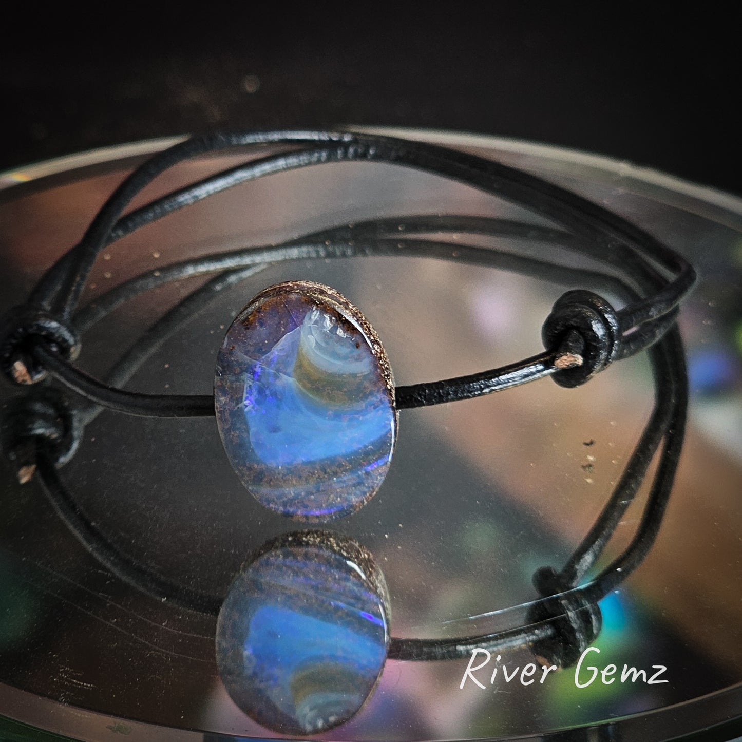 Oval shaped Queensland boulder opal drilled through with leather cord tied to create a bracelet.