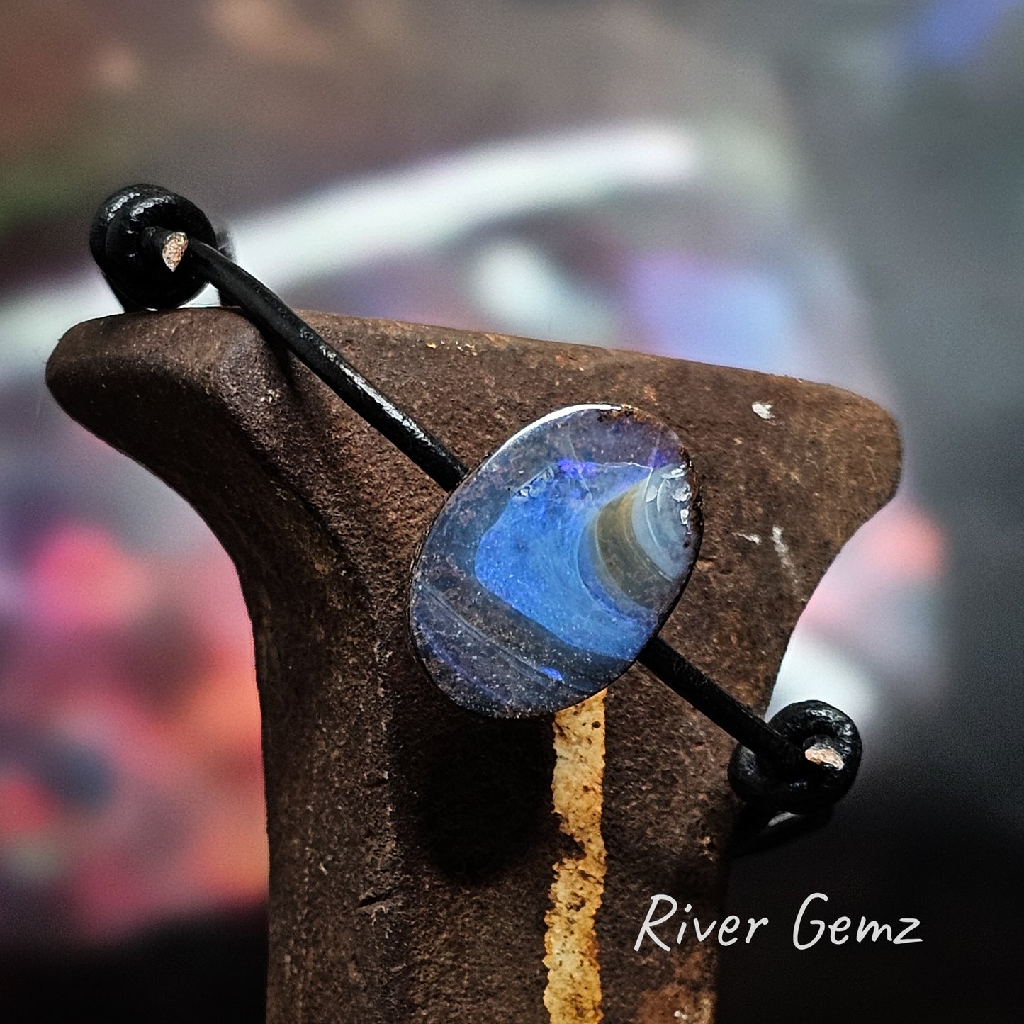 Oval shaped boulder crystal opal with swirls of blue and white on an black leather bracelet.