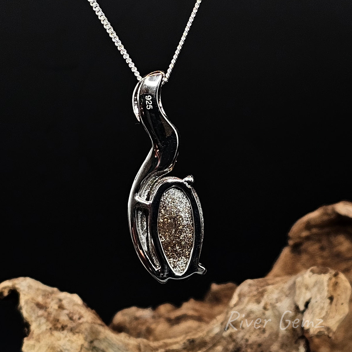 Rear view of a sterling silver pendant necklace with a polished, flowing abstract design showing the ironstone matrix of the boulder opal set in it, suspended from a silver chain against a black background with a piece of driftwood at the bottom.