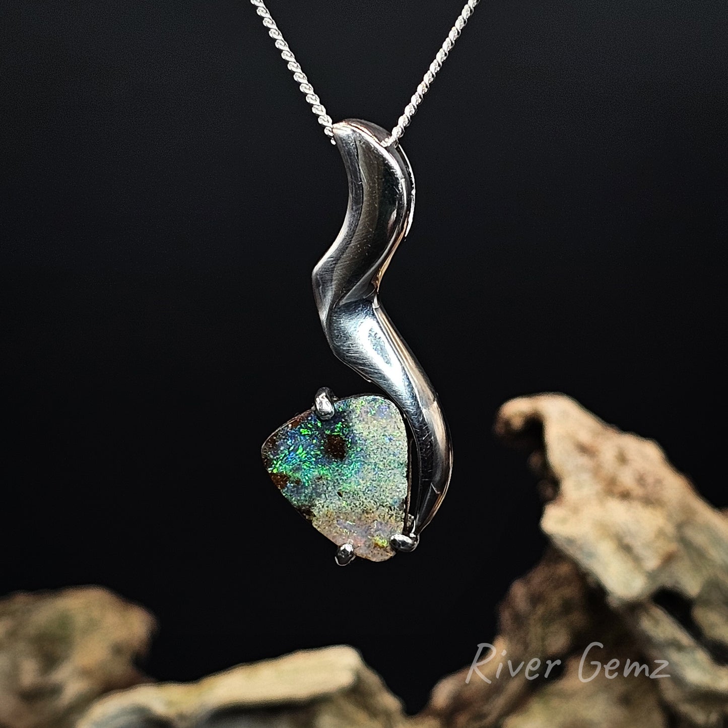 Rounded corner triangular shaped boulder opal set in silver necklace against a dark background.