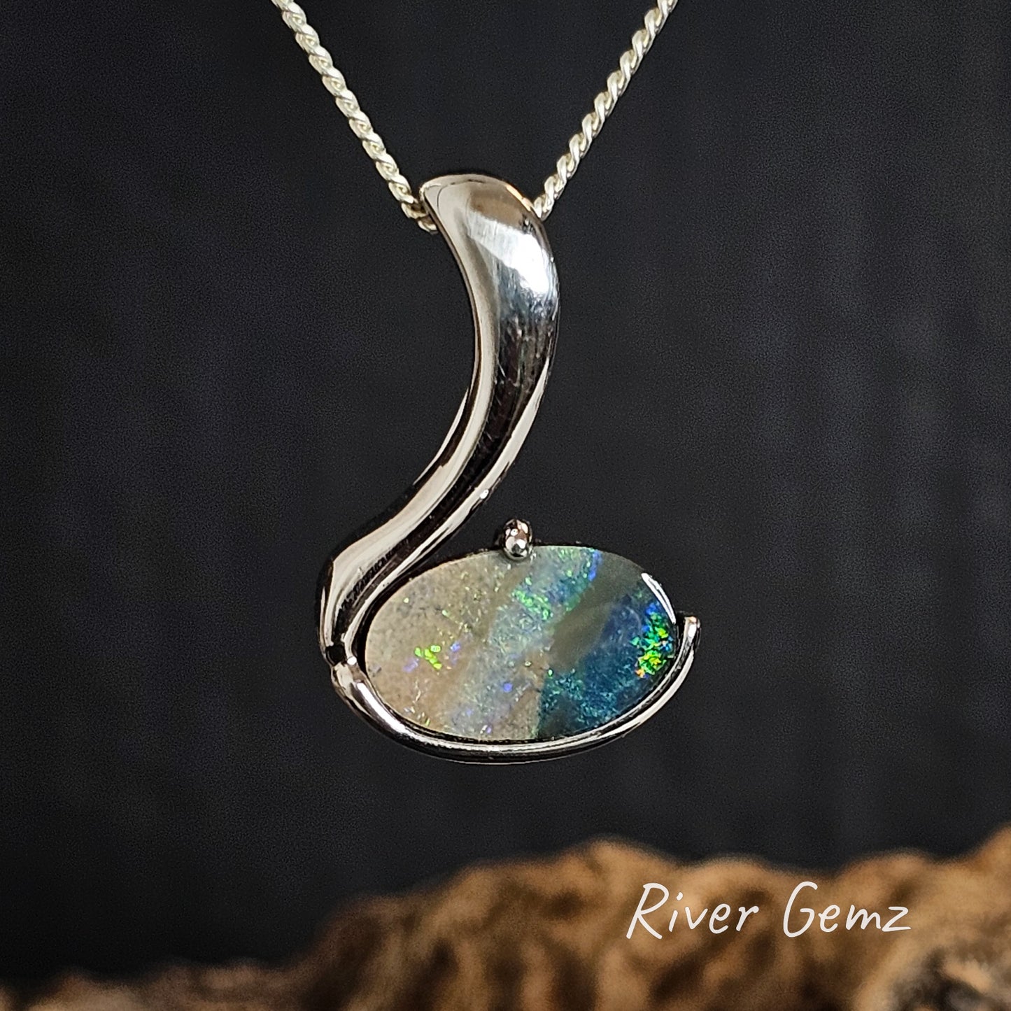 Silver pendant with a colorful gemstone on a dark background, branded 'River Gemz'.