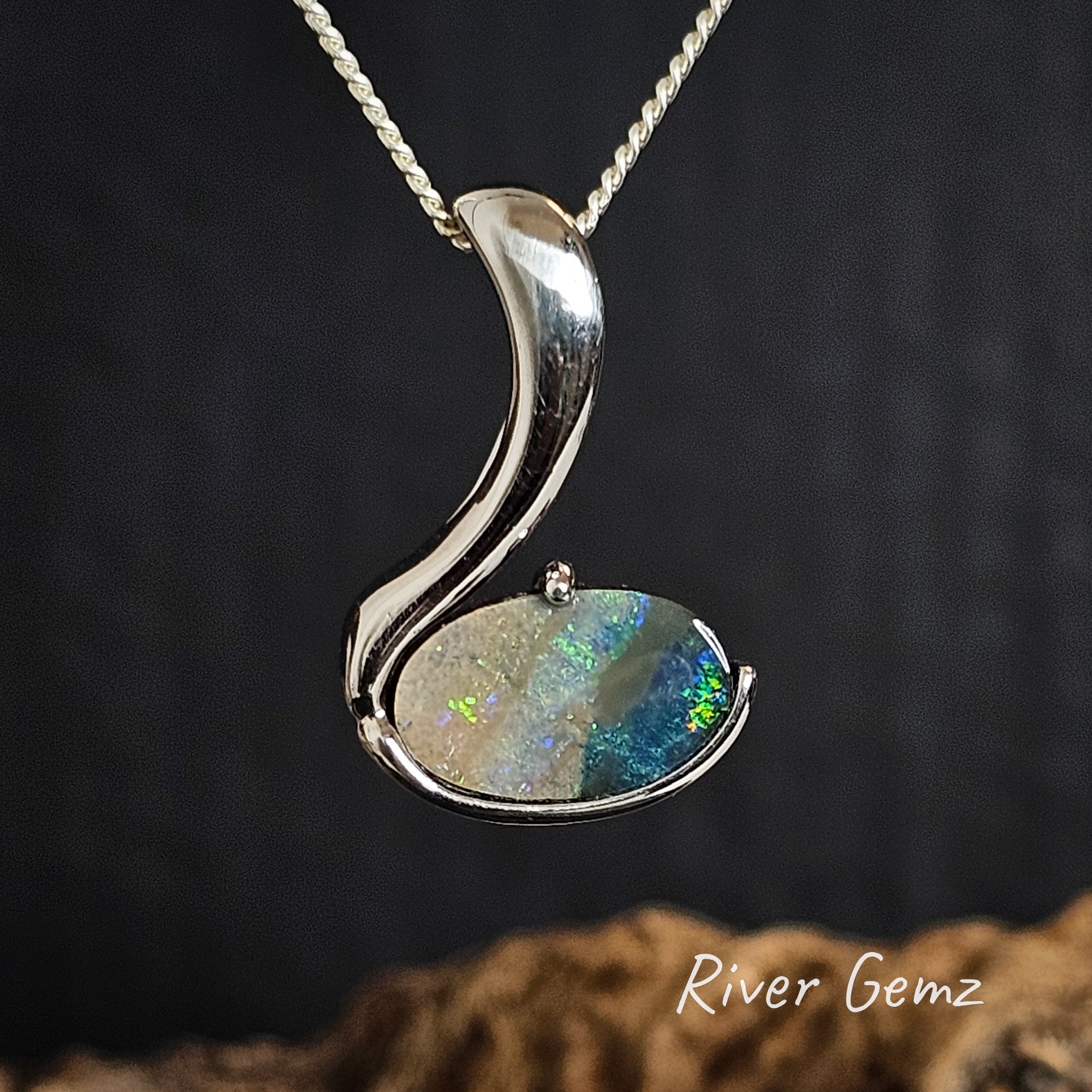 Silver pendant with a colorful gemstone on a dark background, branded 'River Gemz'.