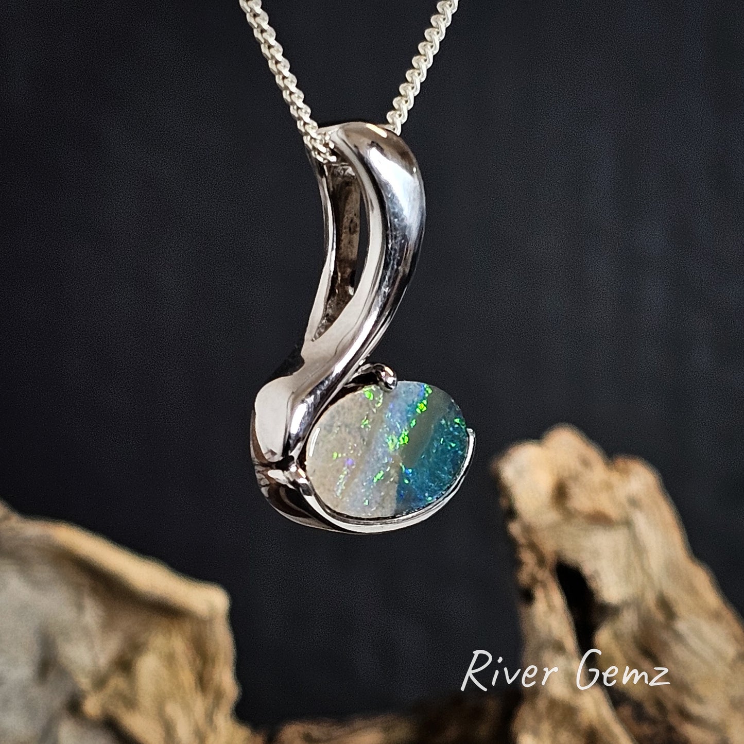 Silver pendant with a blue and green oval shaped boulder opal on a dark background, featuring 'River Gemz' branding.
