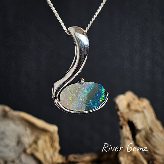 Silver pendant with a colorful gemstone on a dark background, featuring 'River Gemz' branding.
