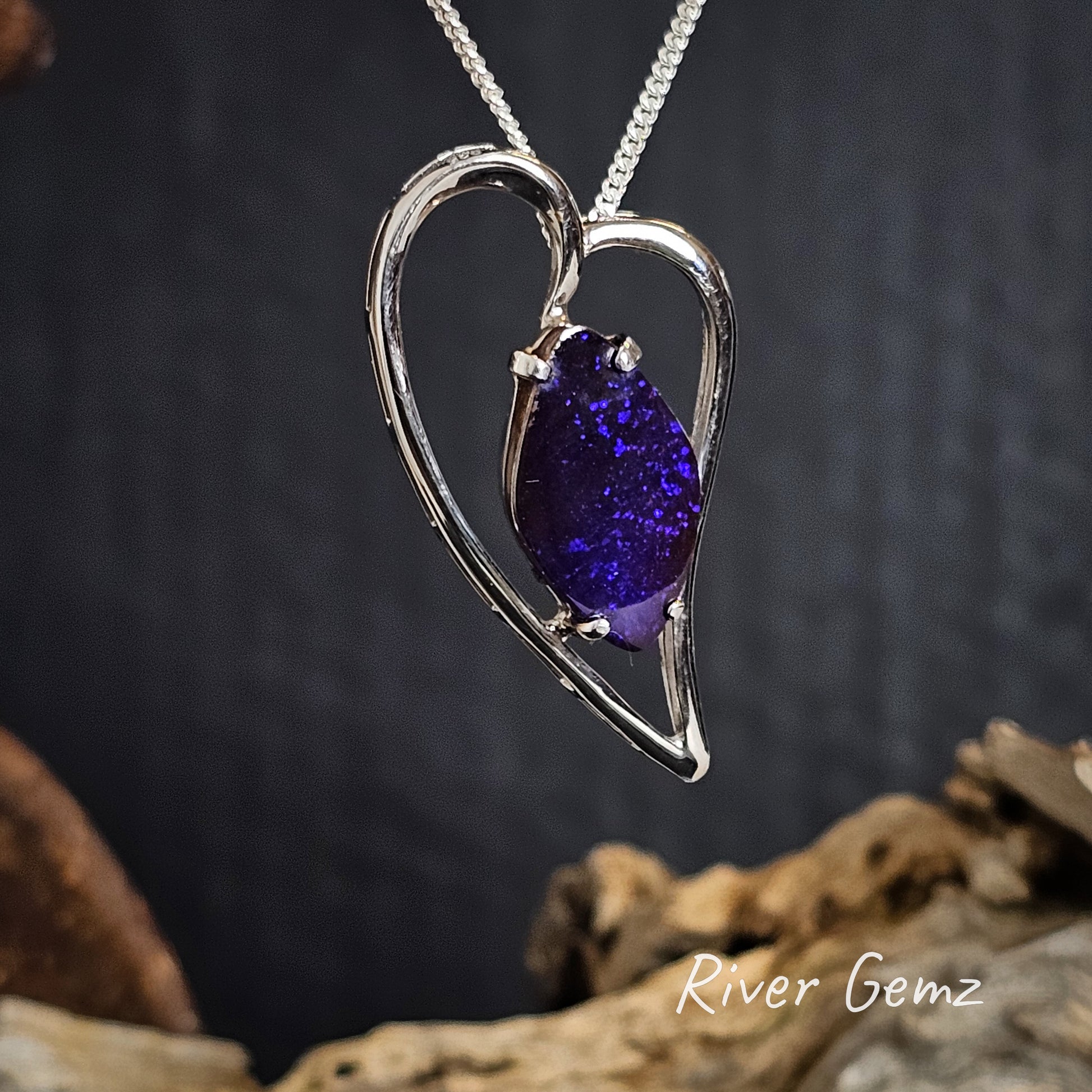 Heart-shaped silver pendant with a purple gemstone on a dark background