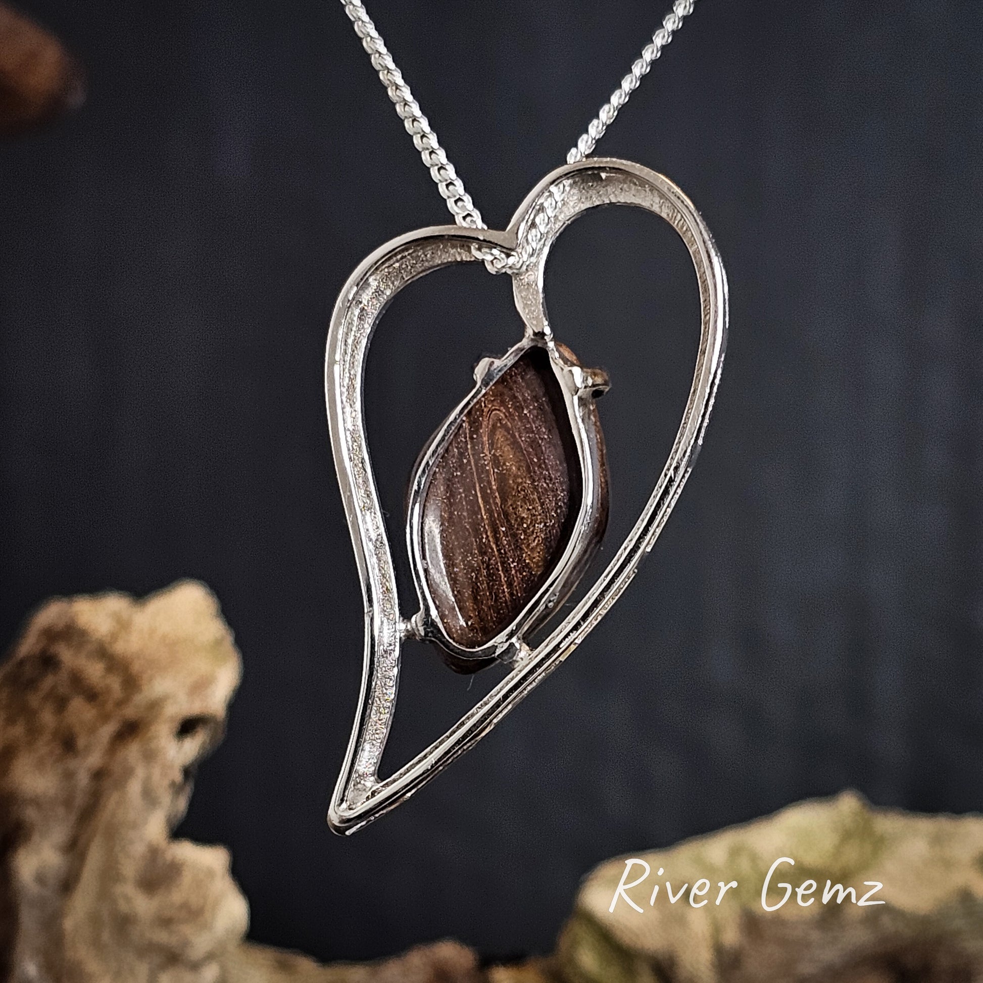 Back of the heart-shaped silver pendant showing the brown ironstone matrix of the embedded boulder opal on a dark background, featuring 'River Gemz' branding.
