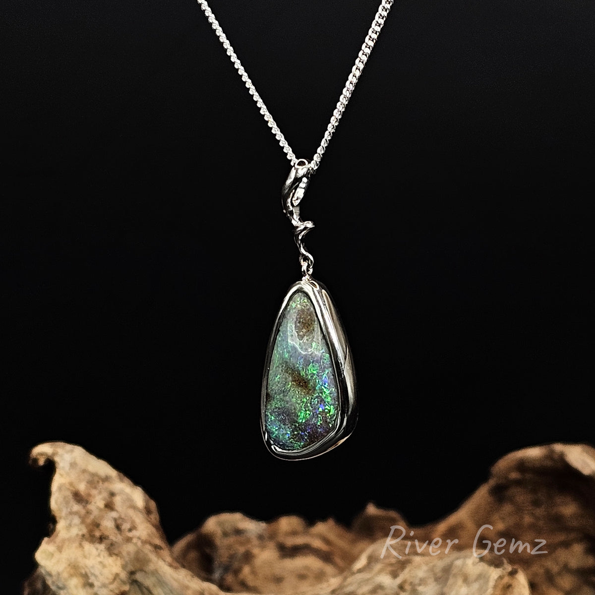 Slightly skewed view of sterling silver pendant showing the unusually shaped bail. Black background, driftwood base and 'River Gemz' water mark in the bottom right hand corner.