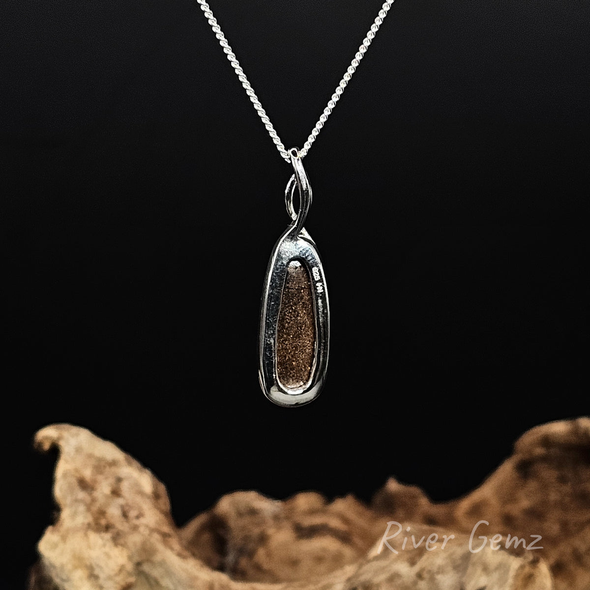 Rear view of the necklace shows the brown base of the boulder opal. Against a black background and above a piece of driftwood with 'River Gemz' watermark in the bottom right hand corner.
