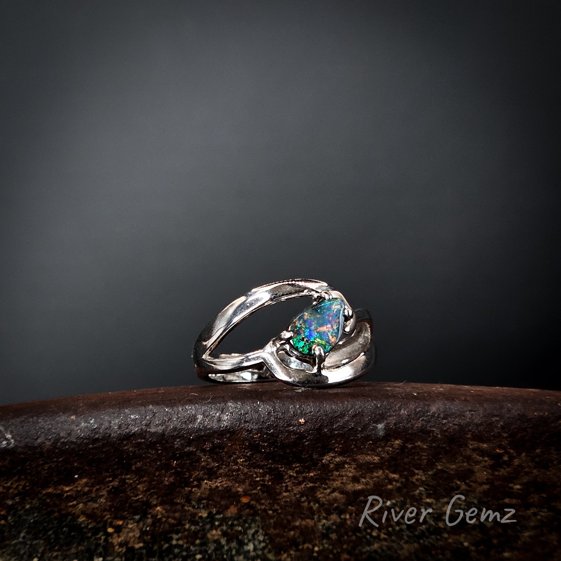 Silver ring with a multi-coloured dark opal on a dark surface, branded 'River Gemz'.