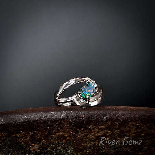 Silver ring with a multi-coloured dark opal on a dark surface, branded 'River Gemz'.