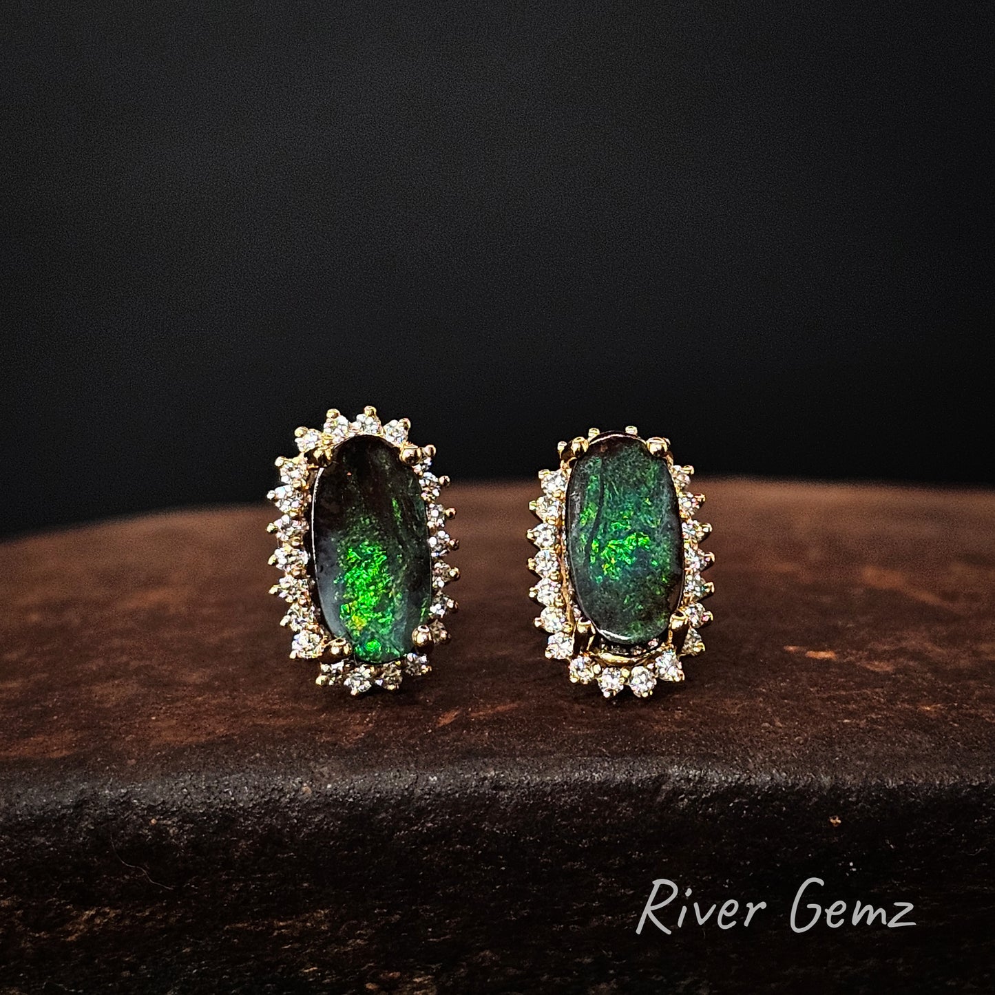 Pair of green gemstone earrings with gold and diamond accents on a dark surface, branded 'River Gemz'.