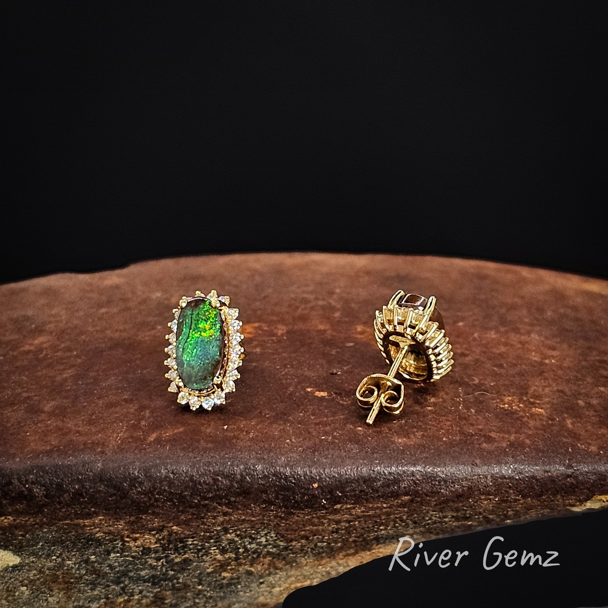 Two gold studs with gemstones on a dark background, featuring the brand 'River Gemz'.