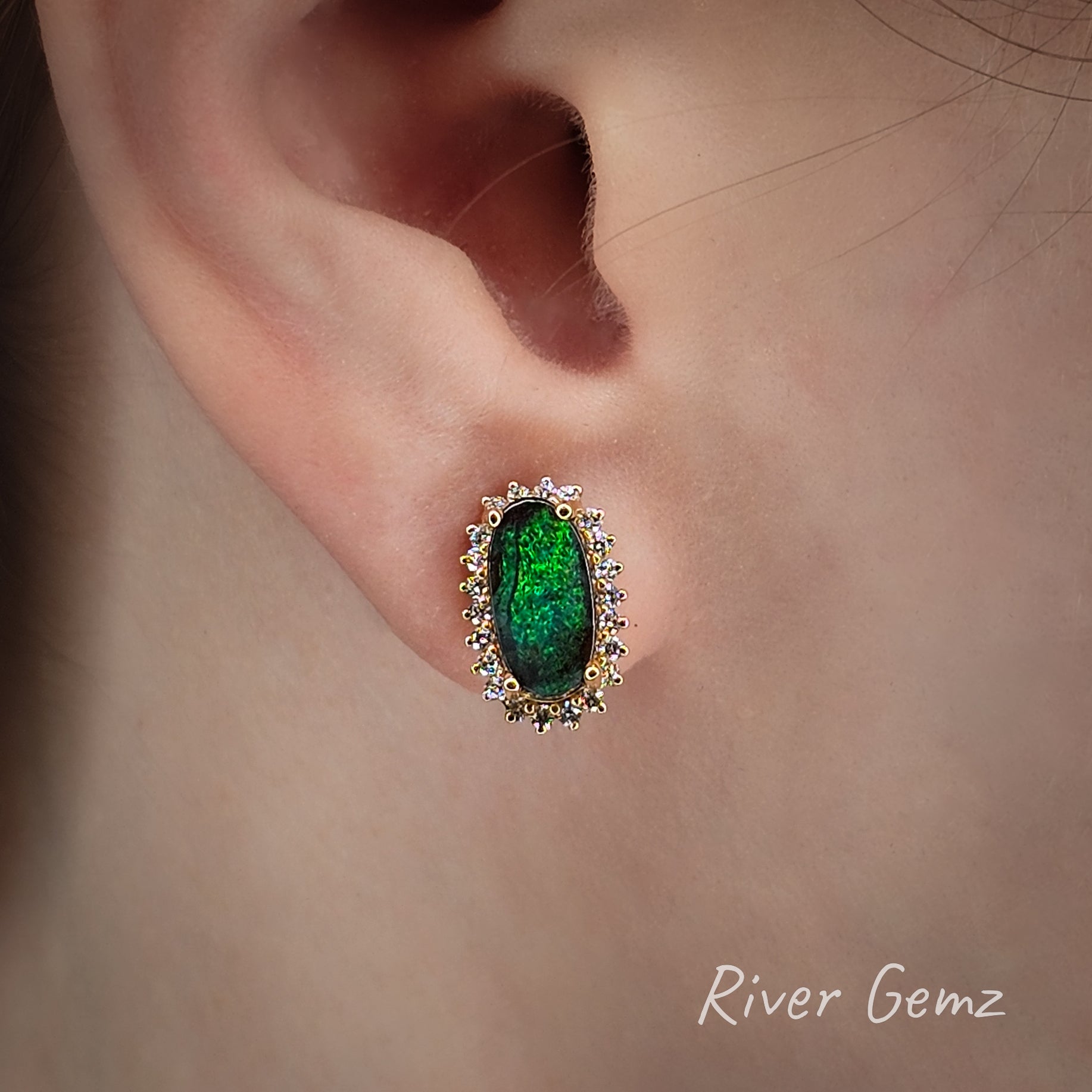 Close-up of a person wearing a green dark opal with diamond surround earring with 'River Gemz' branding.