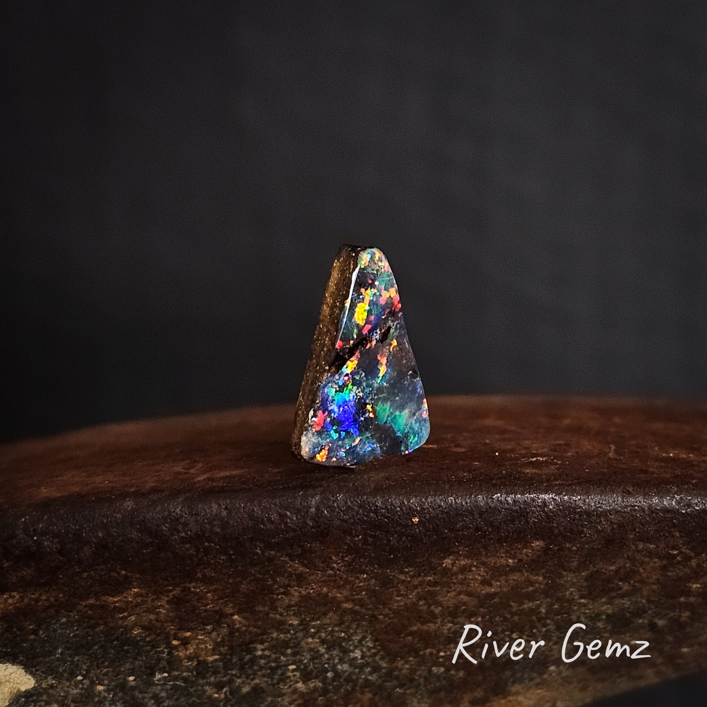 Multicolored opal stone on a dark background with 'River Gemz' branding.