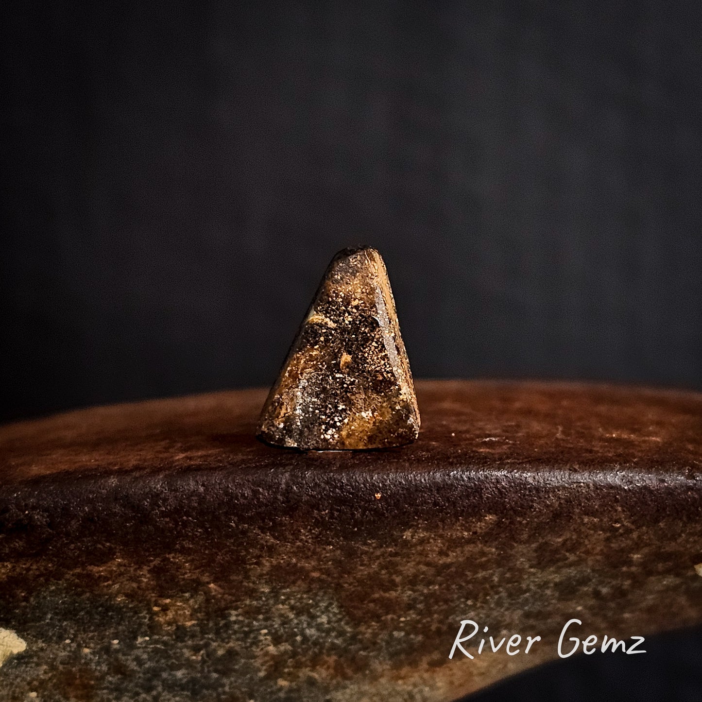 Rear view of the stone showing the ironstone matrix of the boulder opal on a dark surface with 'River Gemz' branding.