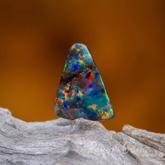 Colourful triangular shaped opal standing on a light grey grained wood.