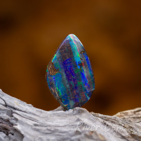 Multicolured dark opal standing on light grey grained wood.