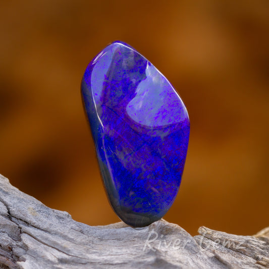 4 images of the shimmering blue opal. This is a front on view. The opal is standing on top of light-grey textured wood and the back drop is a burnt orange colour.