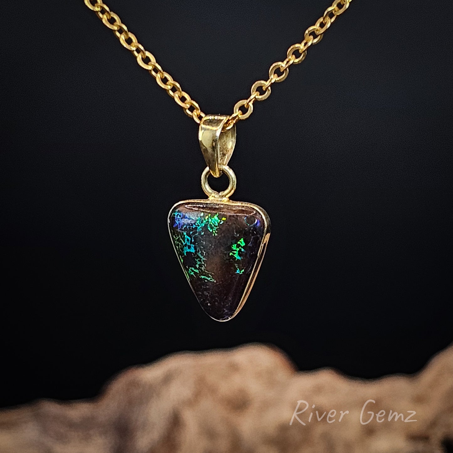 Gold necklace with a triangular pendant on a dark background, featuring 'River Gemz' branding.