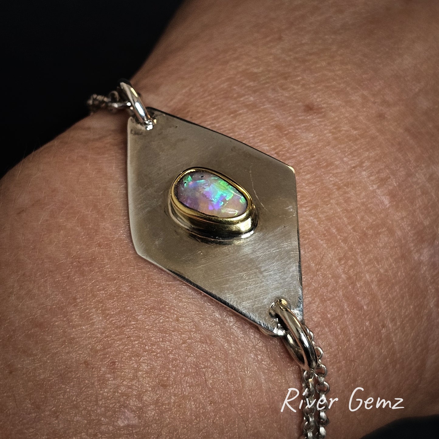 Bracelet with an opal stone on a wrist, branded 'River Gemz'.