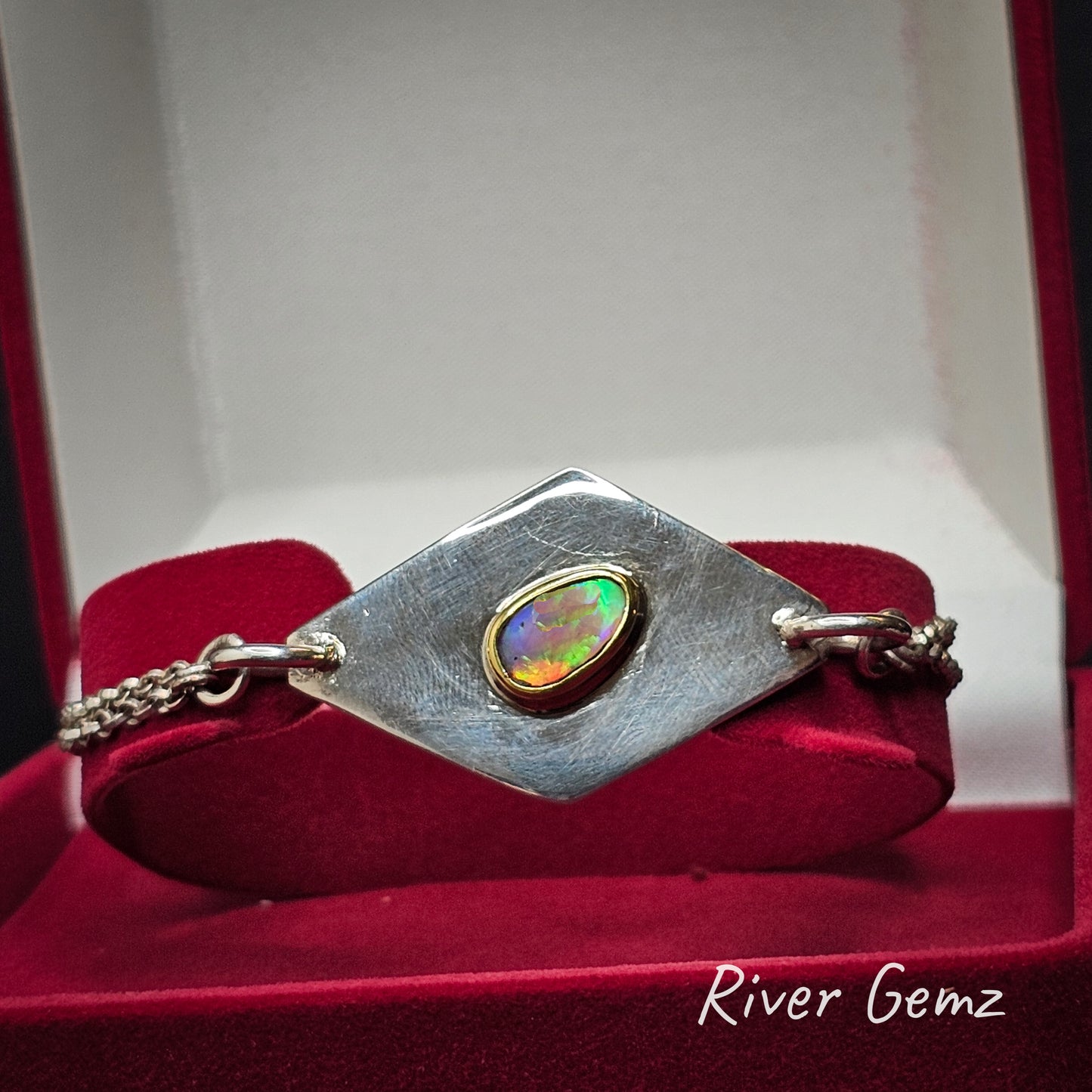 Silver bracelet with a colorful gemstone in a red velvet jewellery box, featuring 'River Gemz' branding.