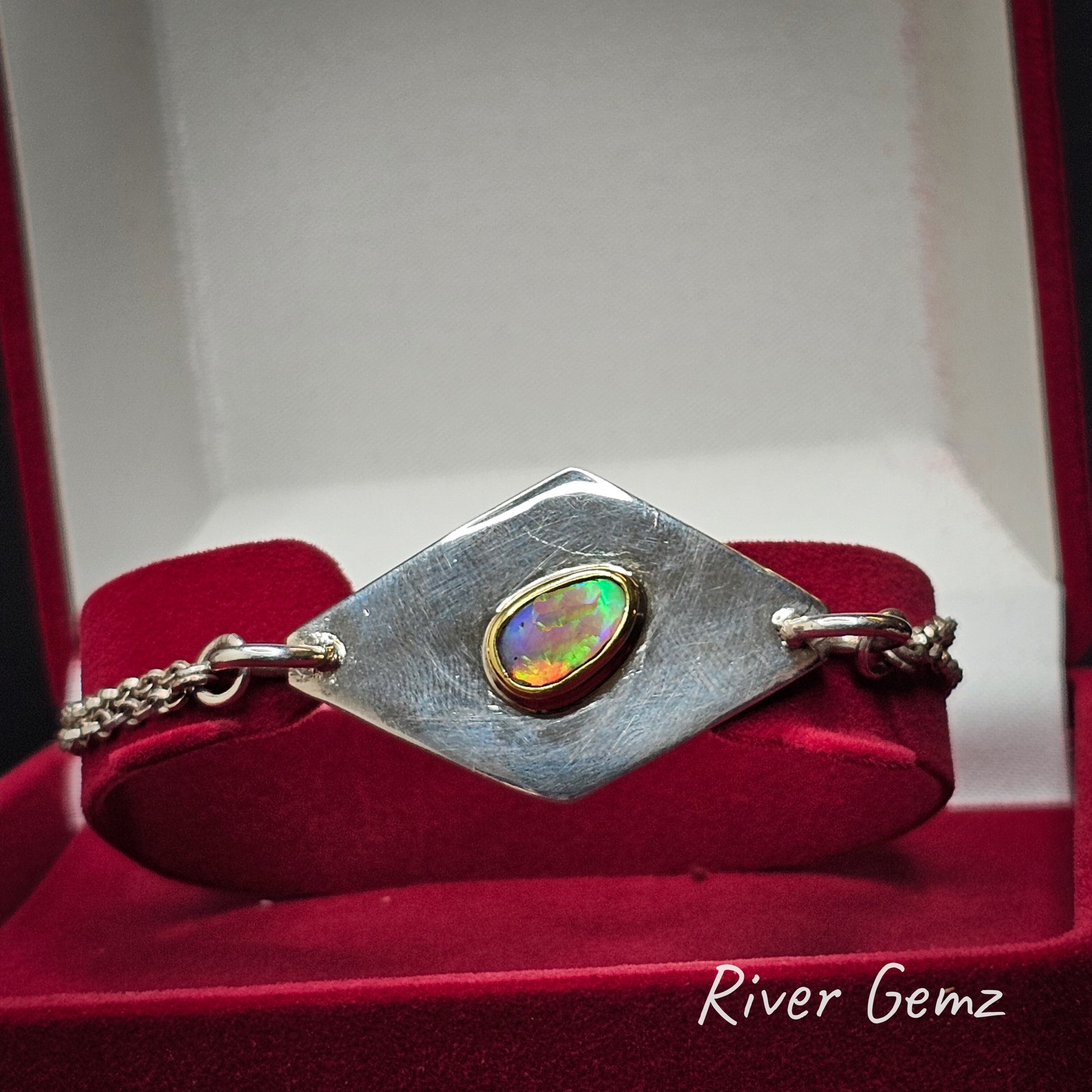 Silver bracelet with a colorful gemstone in a red velvet jewellery box, featuring 'River Gemz' branding.