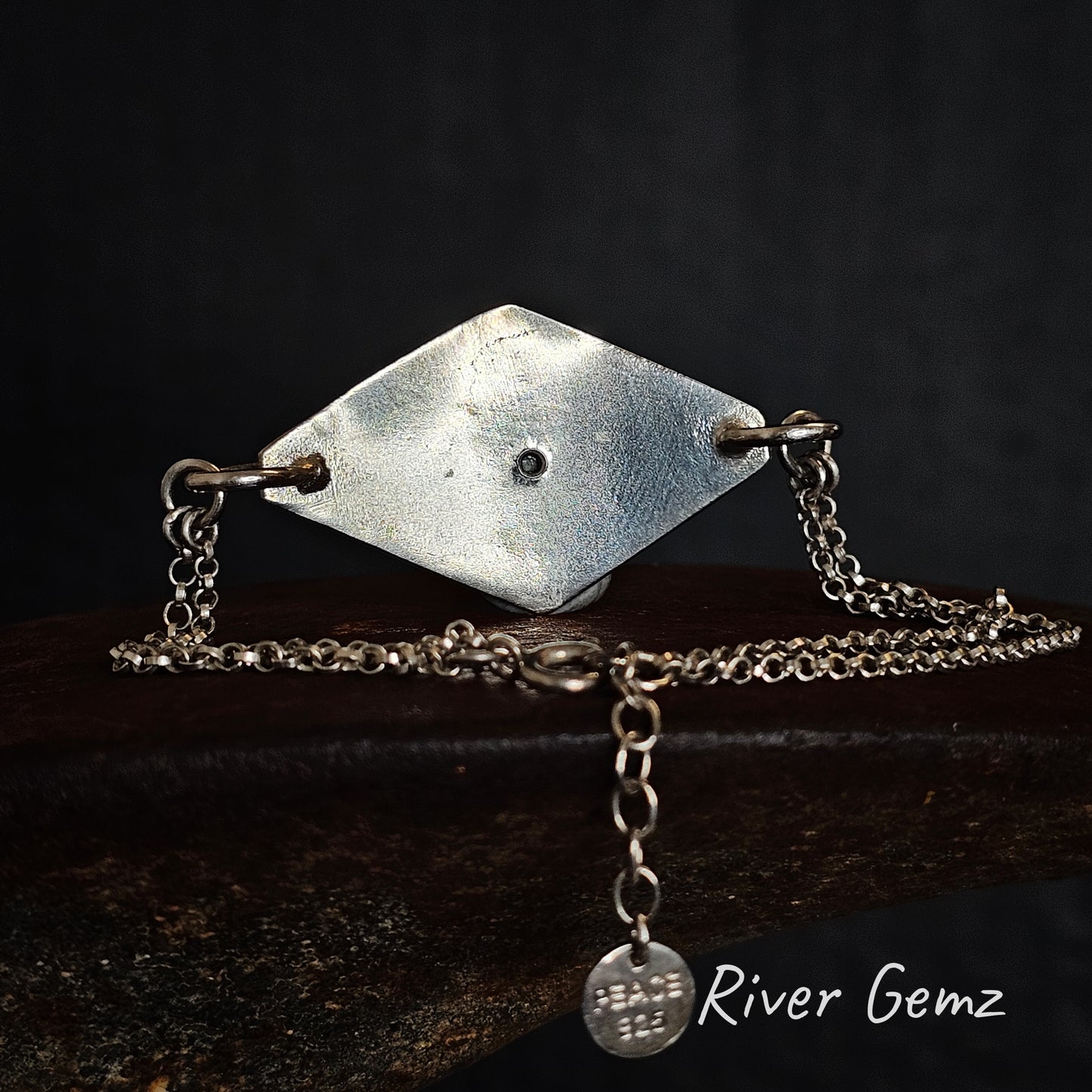 Rear view of silver geometric bracelet with chain on a dark background, featuring 'River Gemz' branding.