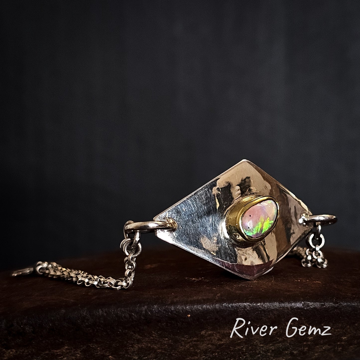 Gold and silver bracelet with a gemstone on a dark background, branded 'River Gemz'.