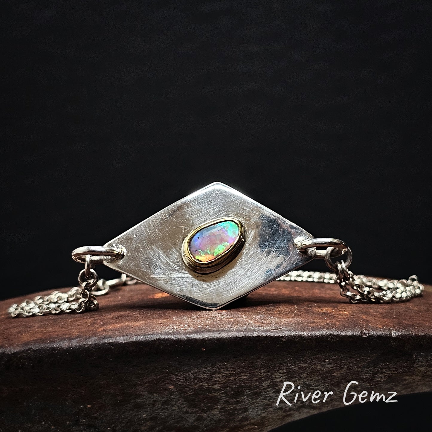 Gold and silver bracelet with a colorful gemstone on a dark background, featuring 'River Gemz' branding.