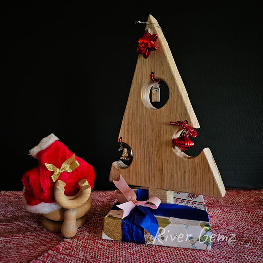 A decorated pine tabletop Christmas tree shown on a red and white table cloth together with a wooden moose head complete with Santa's hat.