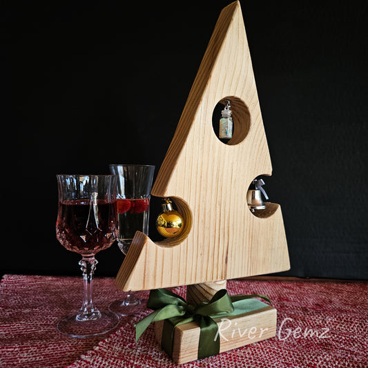 A pine Christmas tree sits on a wooden base resembling a present. The tree includes 3 ornaments. The photo includes 2 crystal glasses for decoration.