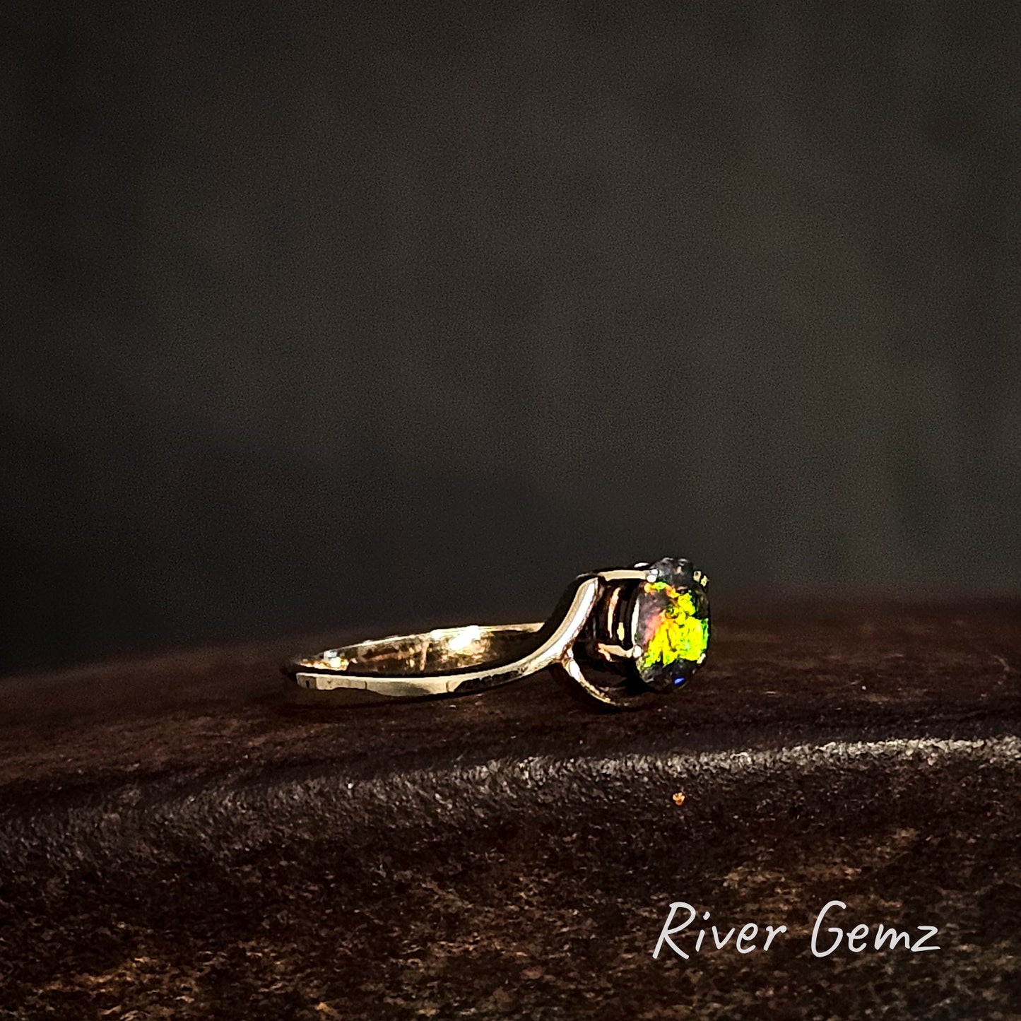 Gold ring with a green gemstone on a dark surface, branded 'River Gemz'.