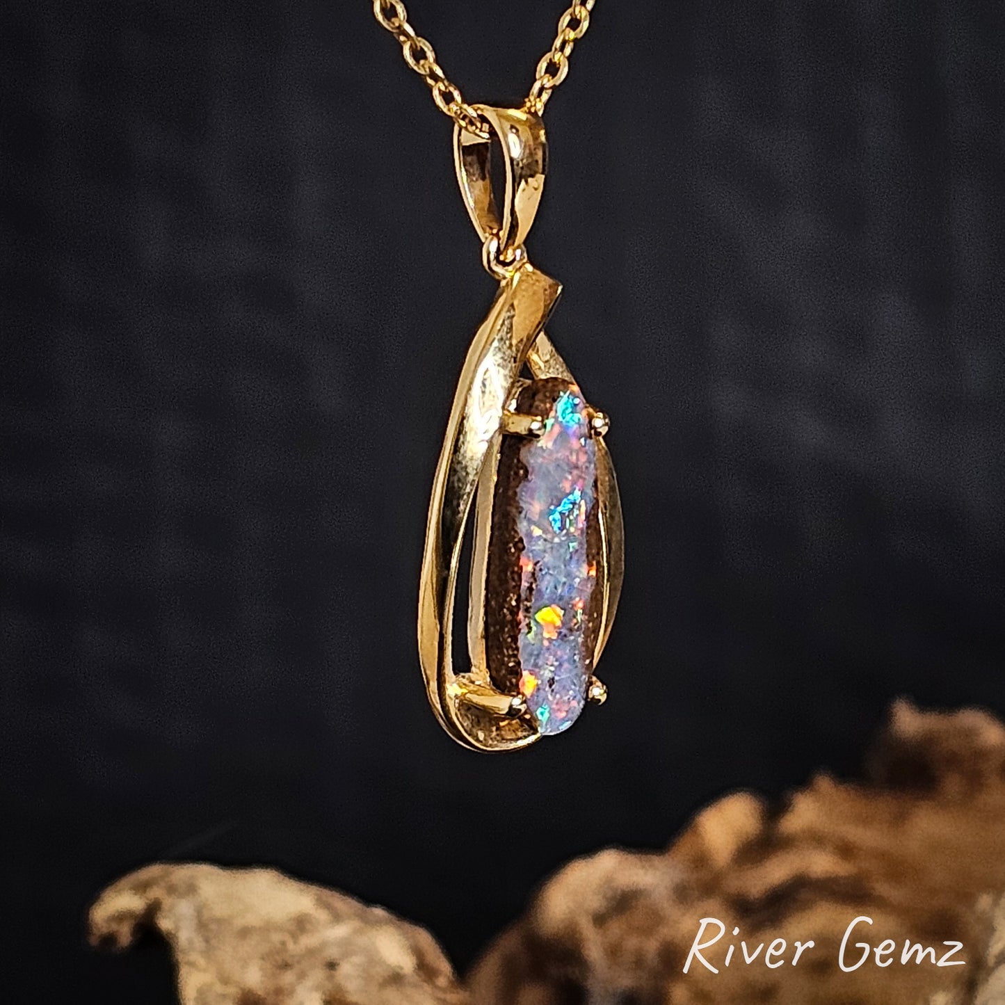 Side view of gold pendant shows the thickness of the boulder opal and the good sized bail on a dark background