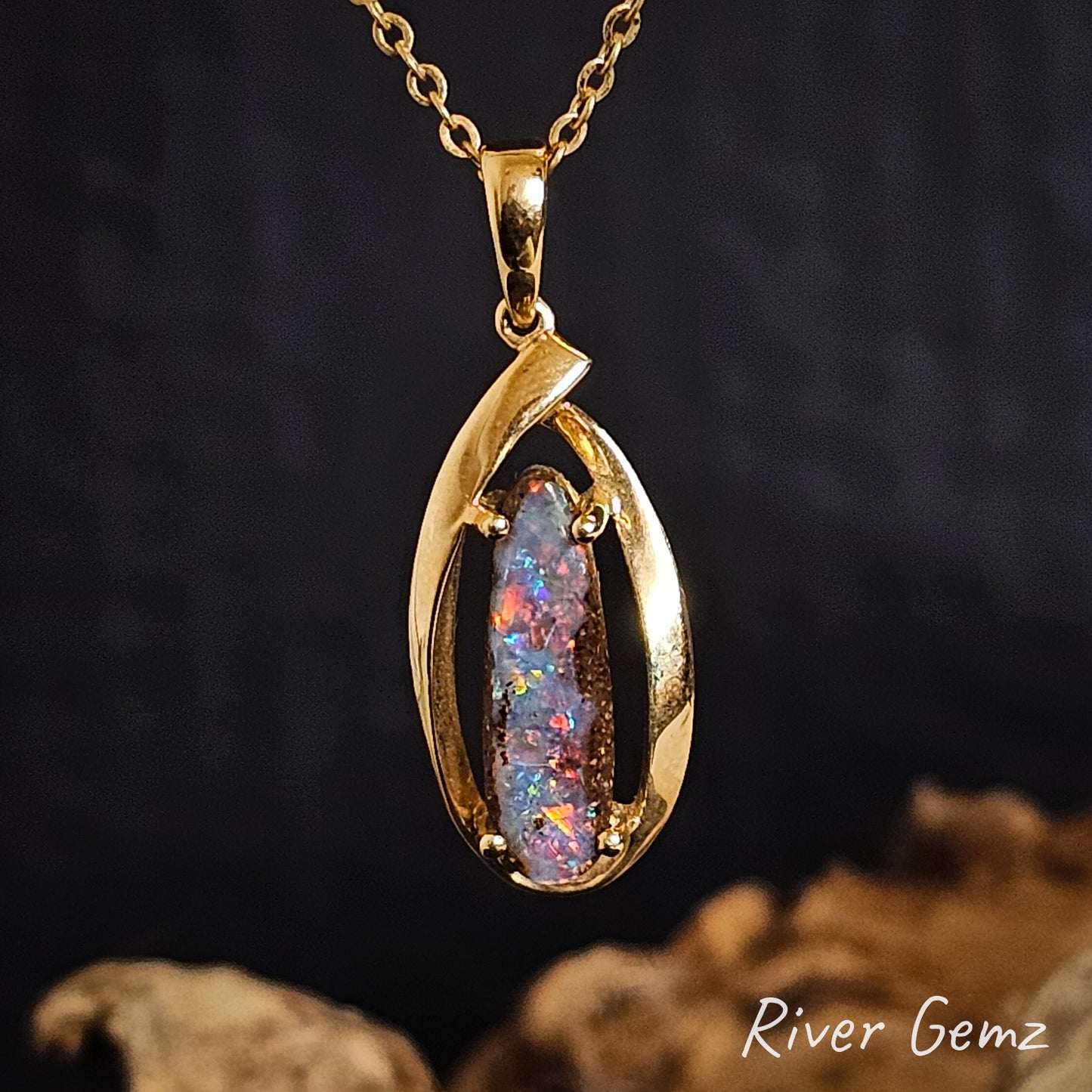 Gold pendant with a colorful boulder opal on a dark background, featuring 'River Gemz' branding.