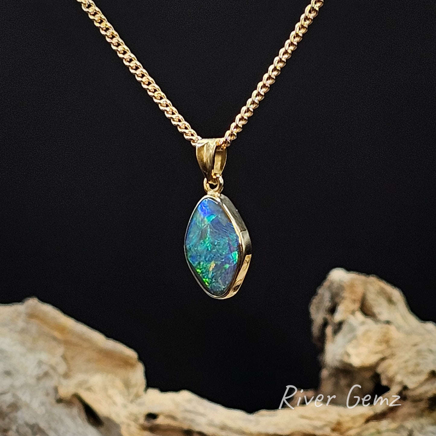 Gold necklace with a blue and green boulder opal on a dark background