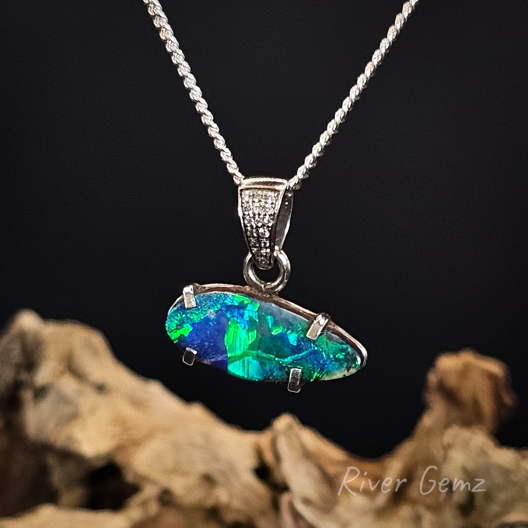 Blue and green leaf shaped boulder opal claw set in a white gold necklace on a dark background with 'River Gemz' branding.