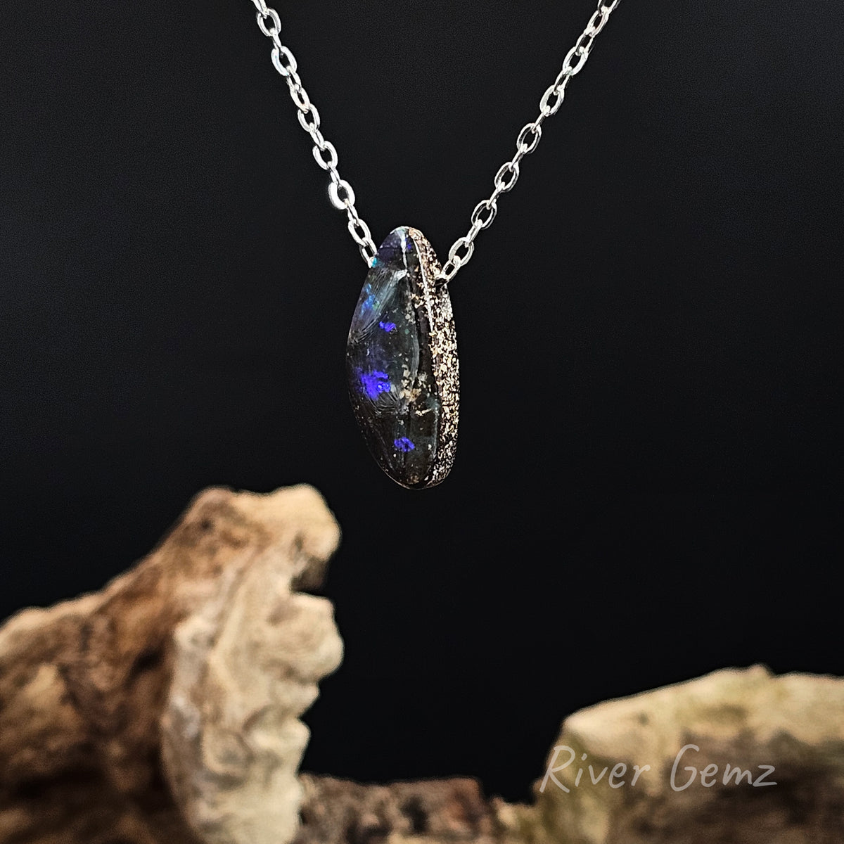 Boulder opal drilled with silver chain passing through it against a black background.