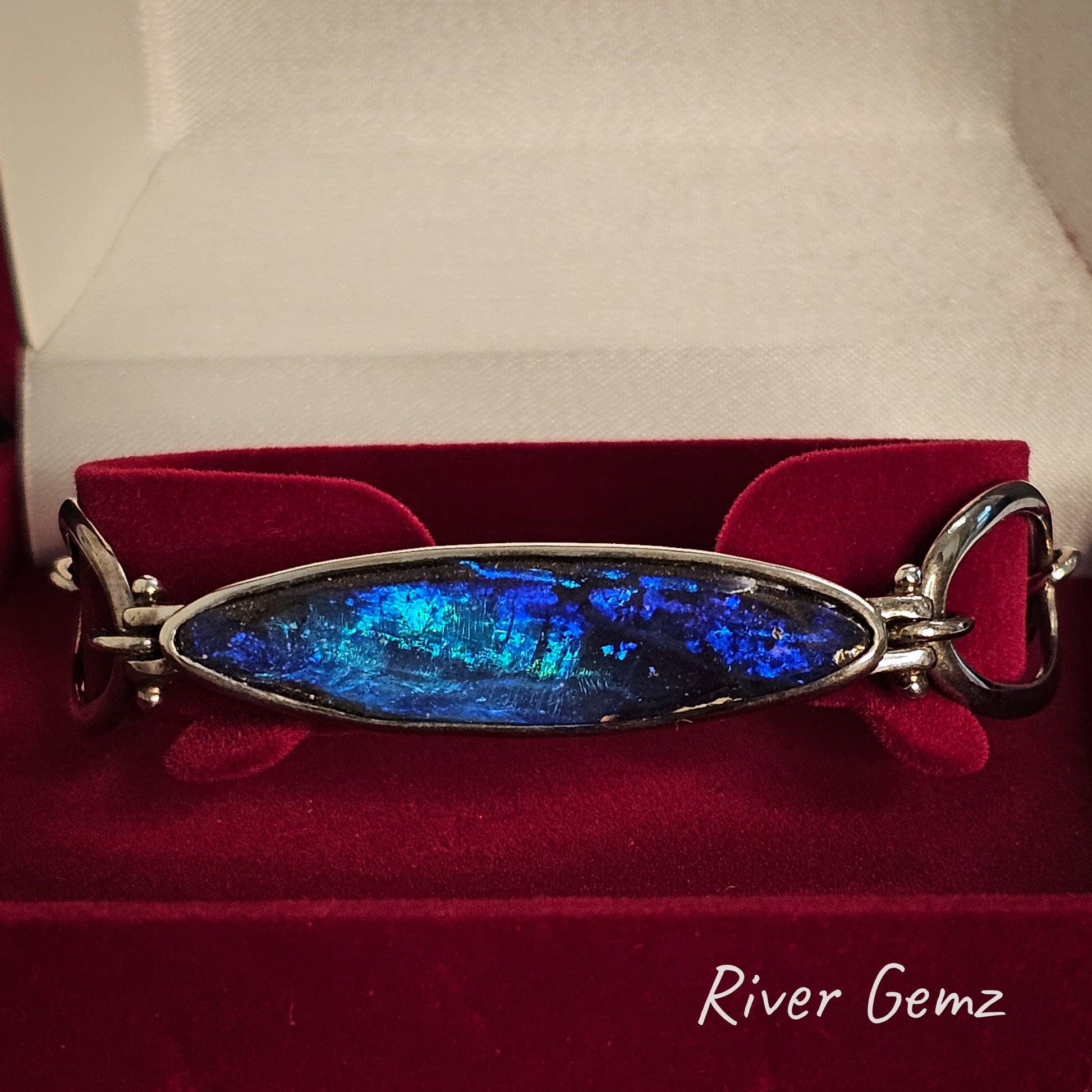 Blue gemstone bracelet on a red velvet cushion with 'River Gemz' branding.