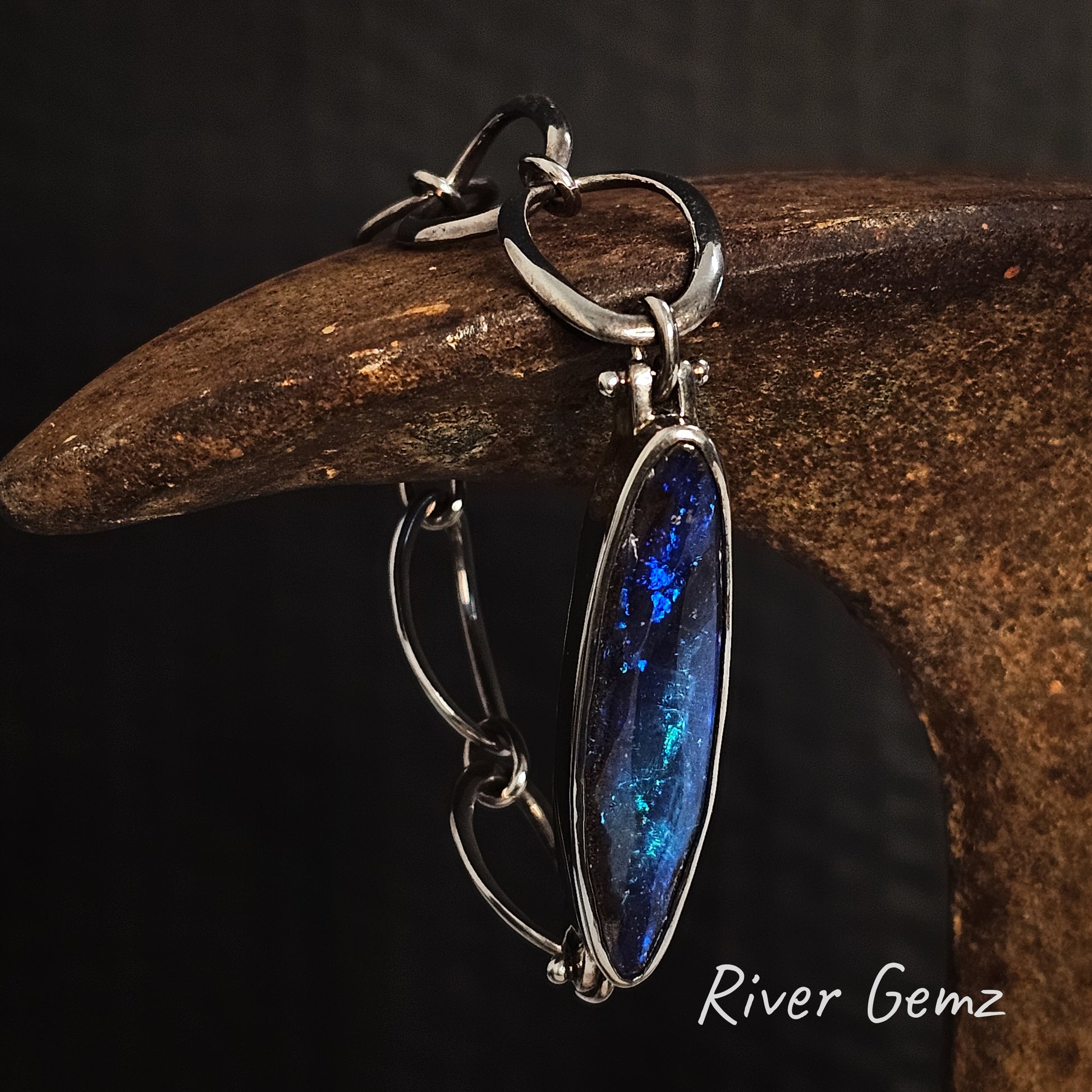 Silver bracelet with large dark blue boulder opal on a dark background, featuring 'River Gemz' branding.