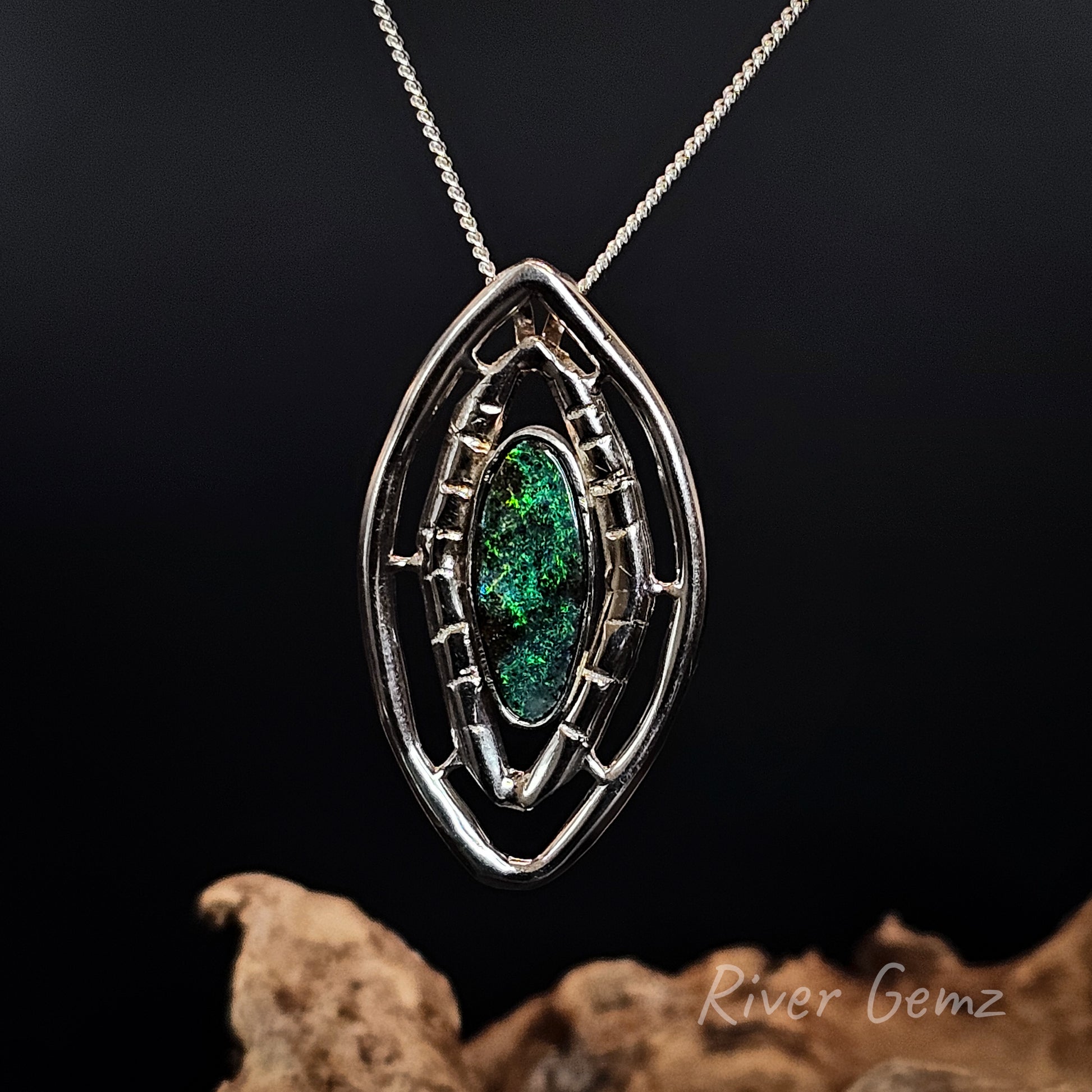Silver pendant with green boulder opal on a dark background