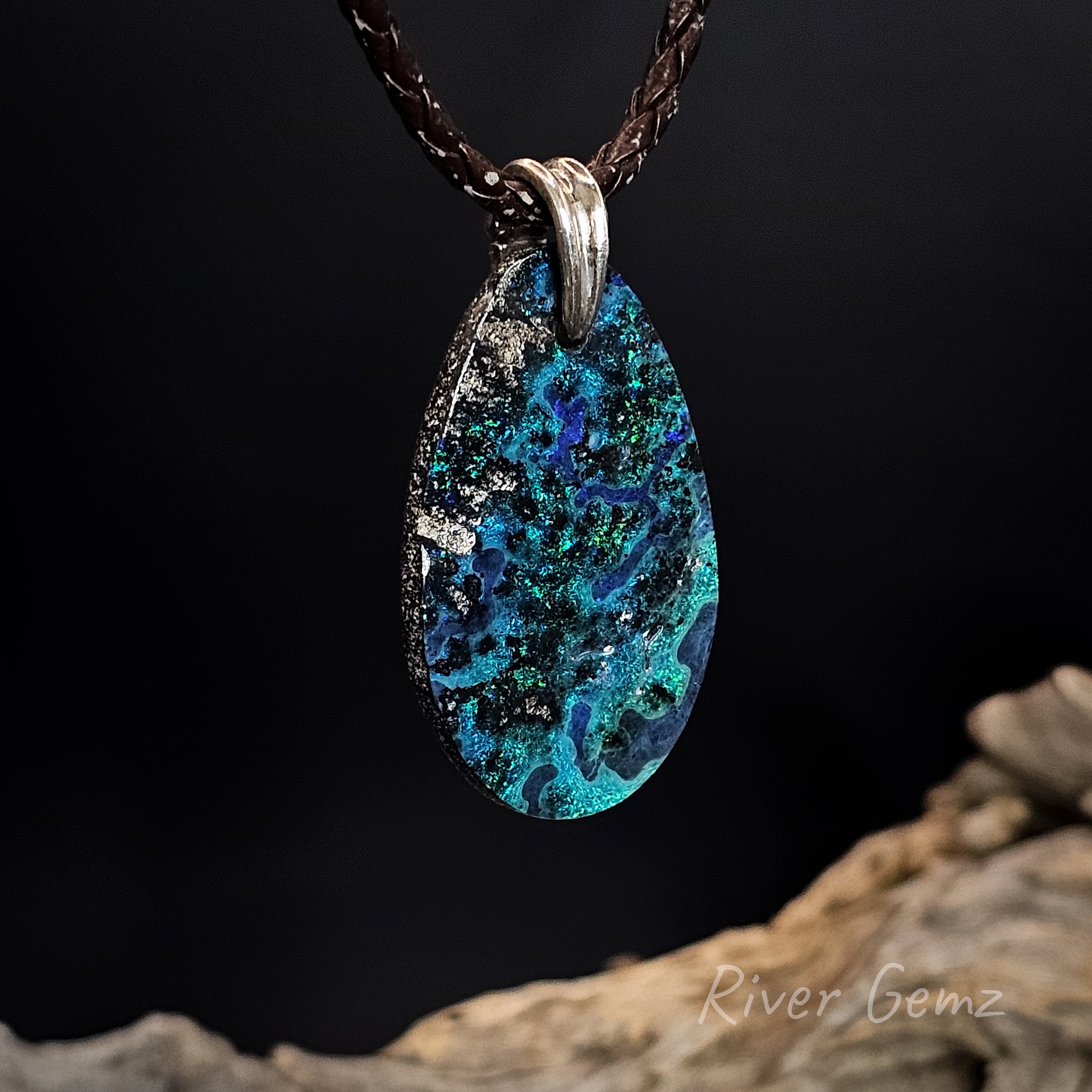 Teardrop-shaped pendant with blue and green patterns on a dark background.