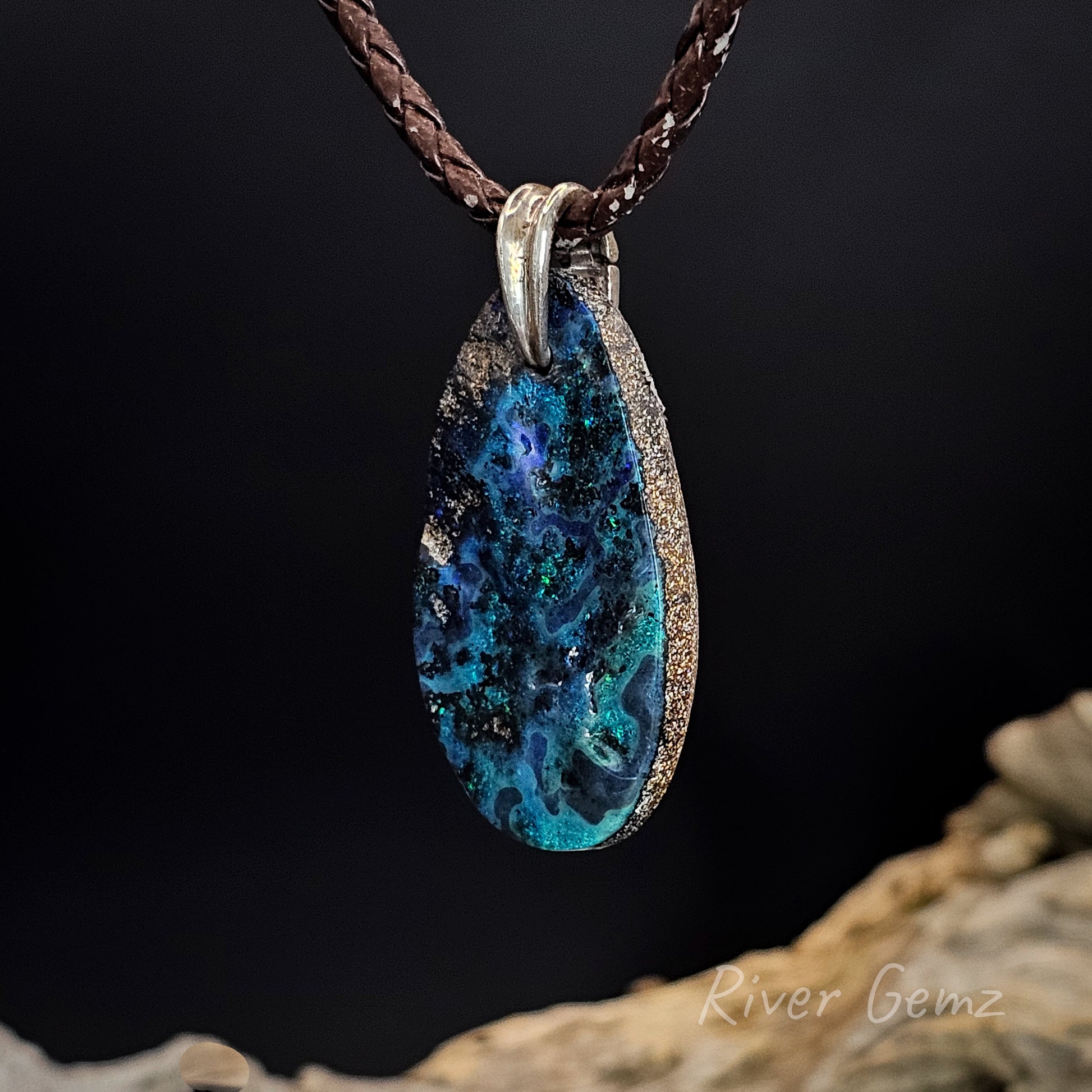 Teardrop-shaped boulder matrix opal  with blue and green design on a leather chain.