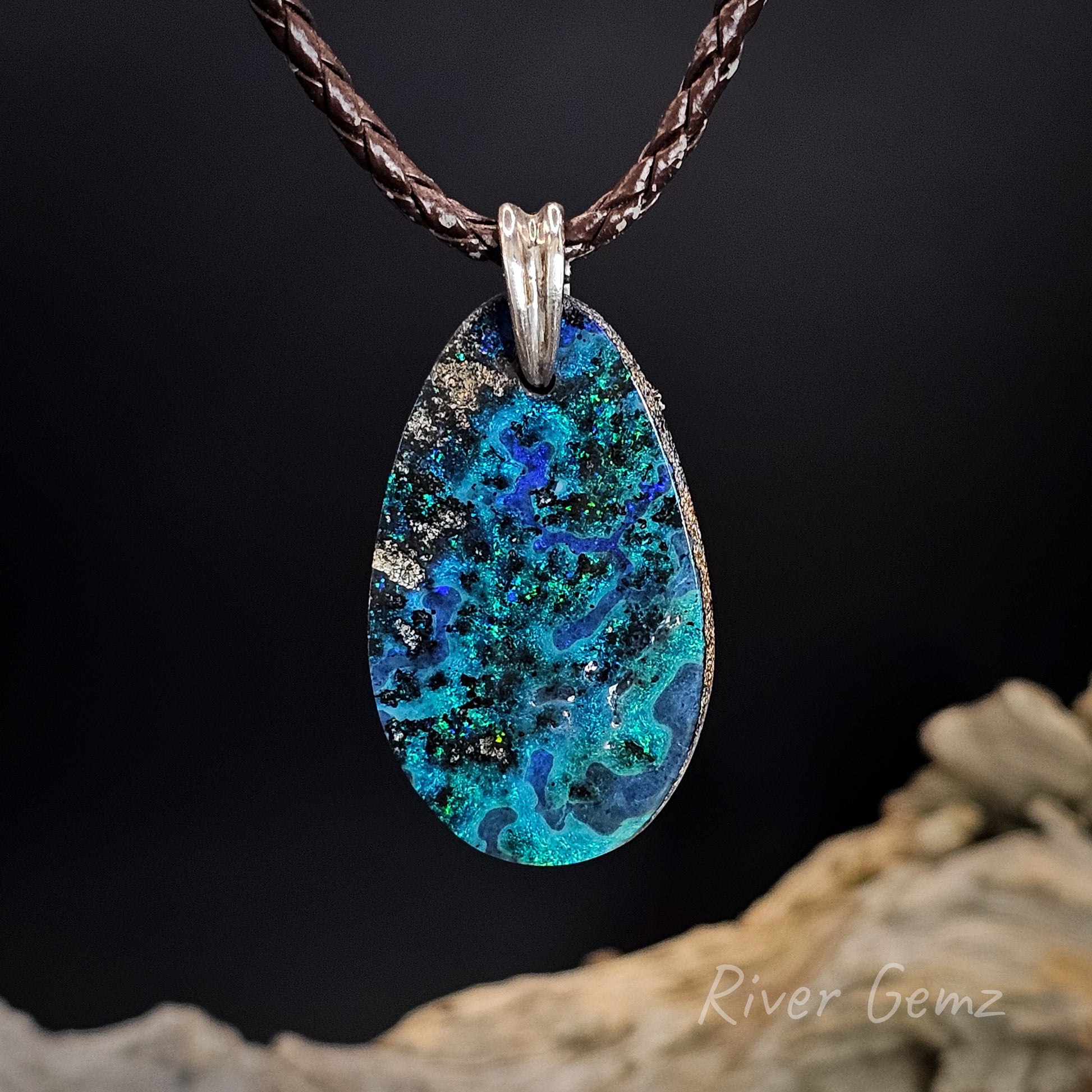 Teardrop-shaped opal opal with blue and green patterns in a necklace on a dark background, featuring 'River Gemz' branding.