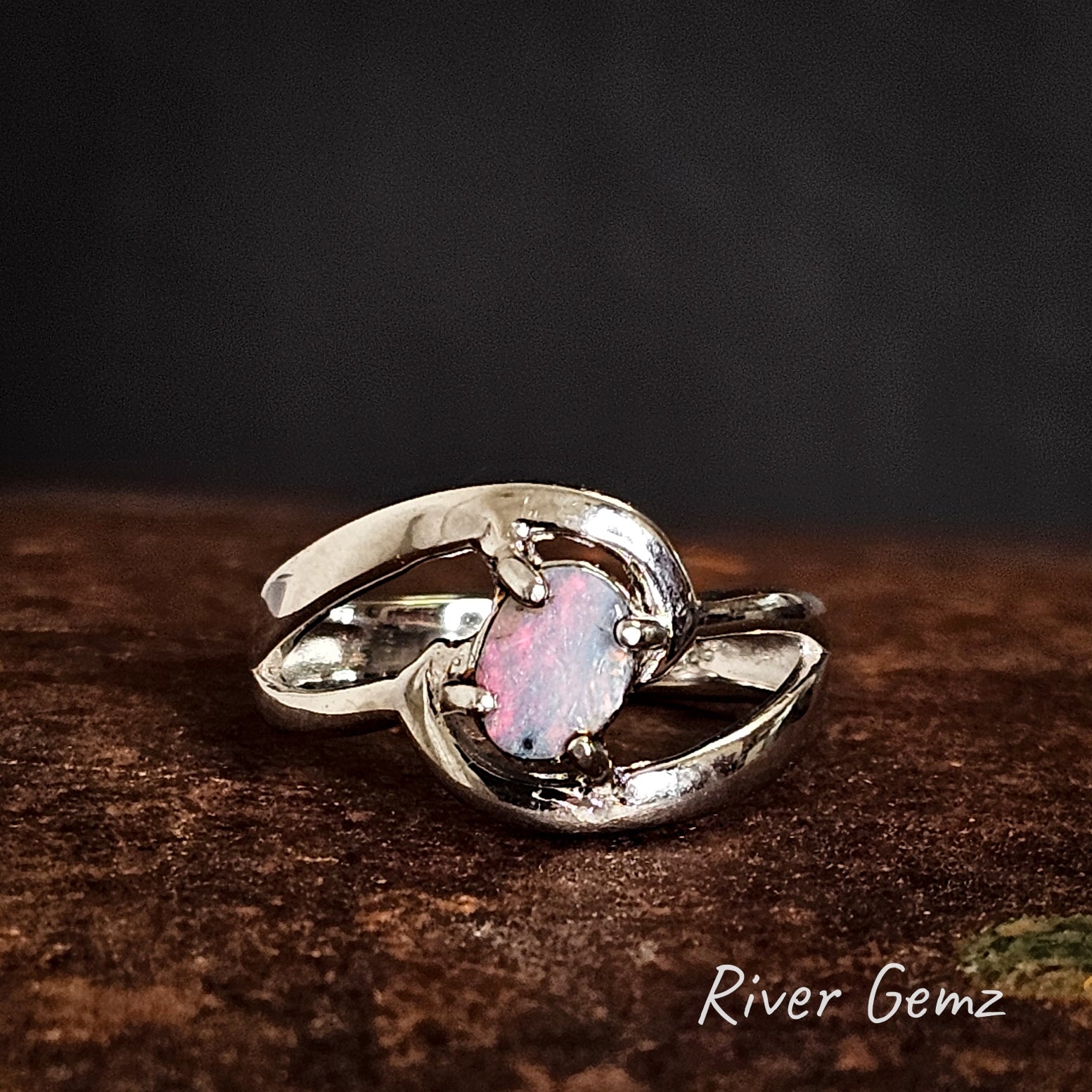 Silver ring with a oval shaped colourful boulder opal on a dark background.