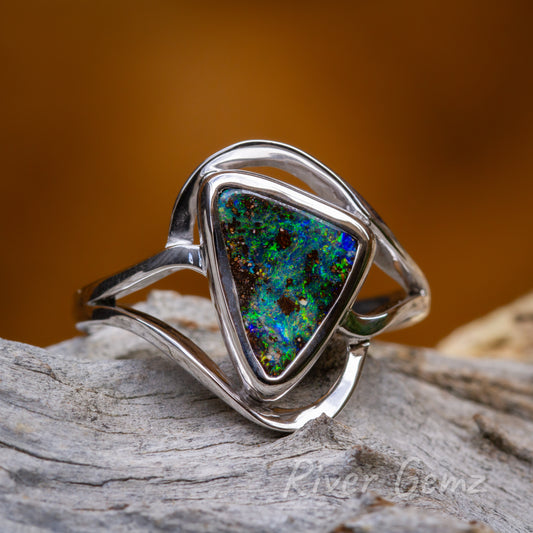 Triangular shaped multi-coloured opal besel set in modern styled silver ring. Ring is pictured on a weathered piece of wood and with a orange/brown backdrop.