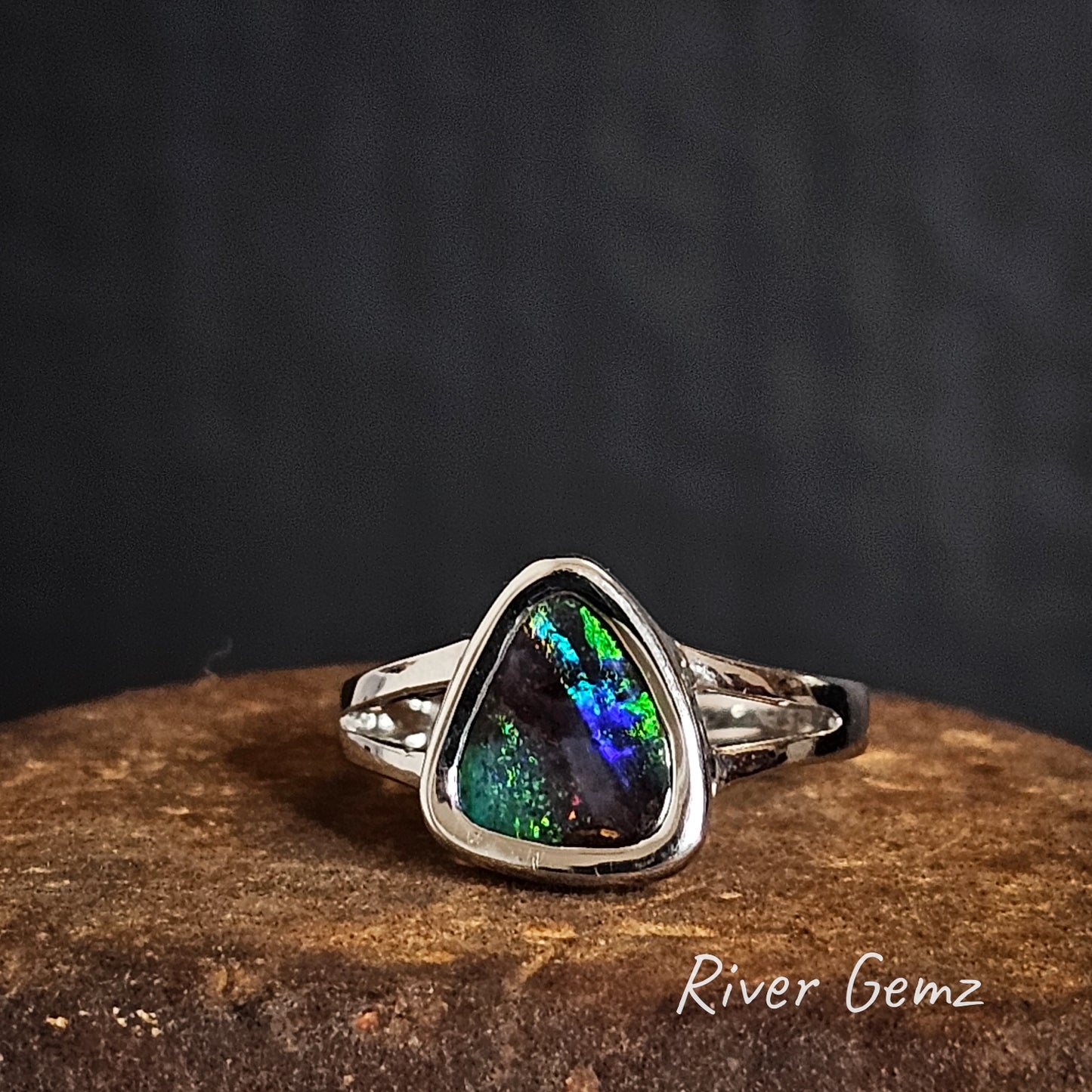 Silver ring with a multi-coloured boulder opal on a dark background, branded 'River Gemz'.