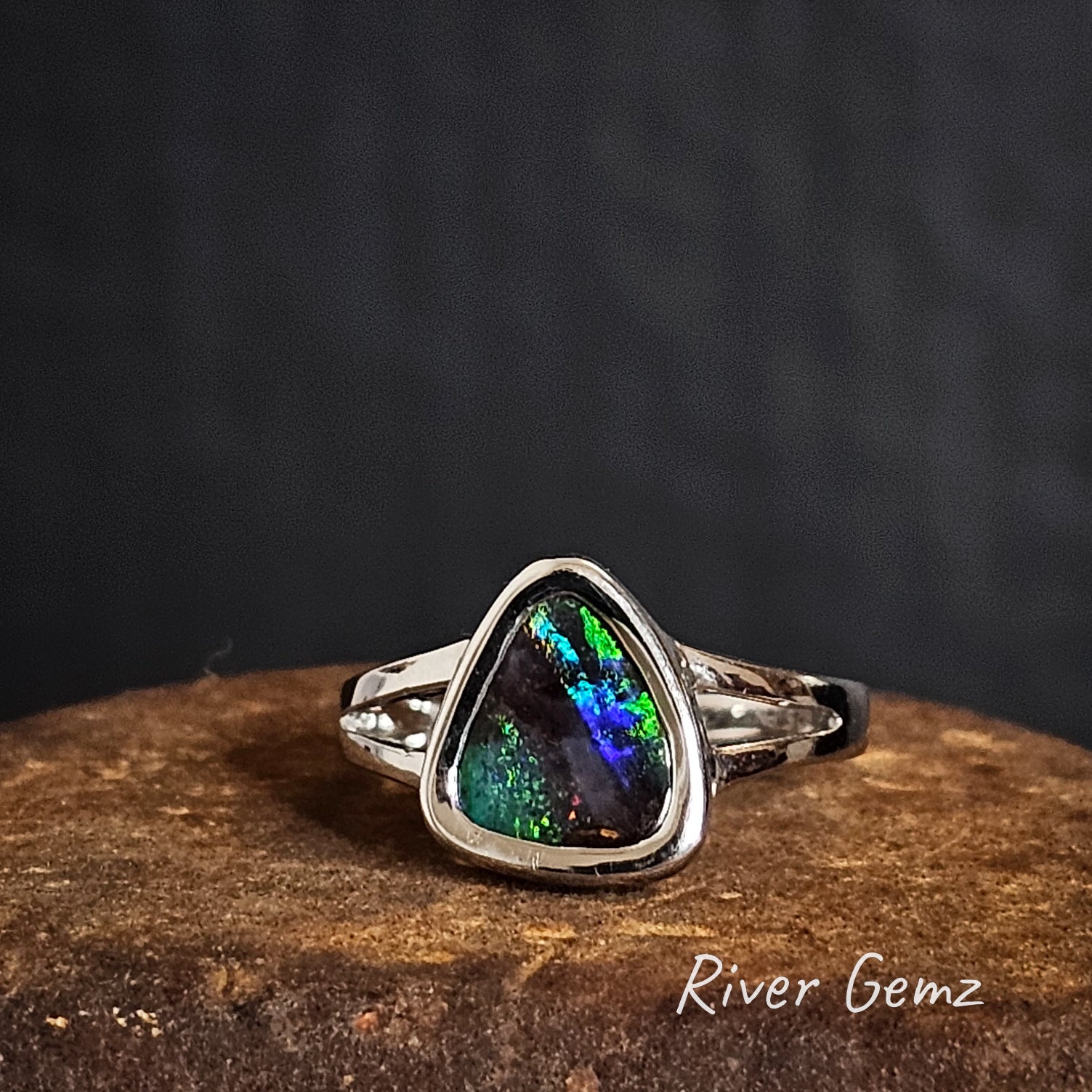 Silver ring with a multi-coloured boulder opal on a dark background, branded 'River Gemz'.